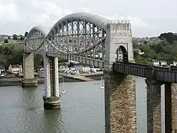 uma ponte atravessando um rio em nível elevado, o tabuleiro apoiado no centro por vigas tubulares metálicas curvas