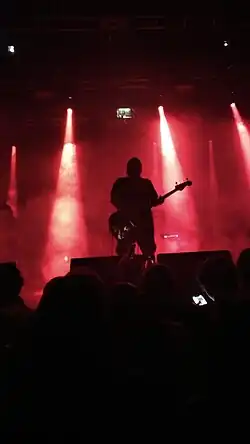 Santiago Motorizado cantando no palco com fundo escuro.