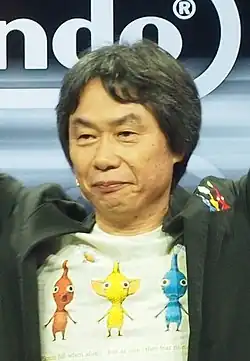 Shigeru Miyamoto, um homem japonês de meia-idade vestindo um blazer espinha de peixe e camisa branca.