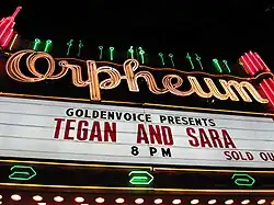Um letreiro neon escrito Orpheum em cima, e escrito embaixo em preto e vermelho "Goldenvoice Presents Tegan and Sara", "SOLD OUT"