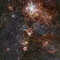A Nebulosa de Tarântula revela uma paisagem cósmica de aglomerados de estrelas, nuvens de gás brilhantes e os restos dispersos de explosões de supernovas.[10]
