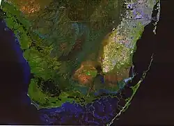 Uma imagem de satélite colorida do sul dos Everglades, da Baía da Flórida, do Oceano Atlântico e do Golfo do México; os Everglades são verdes com grandes secções de água azul, com algumas áreas elevadas castanhas e a ponta mais a sul da Área Metropolitana do Sul da Flórida em branco