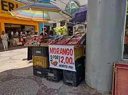 Barraca de vendedor ambulante de morango com placa escrito "Morango - 3 por 12 reais - Aceito pix"