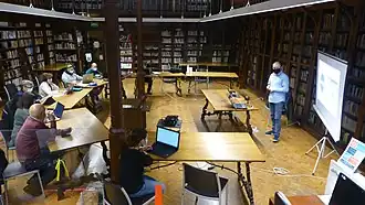 pessoas com computadores participando de evento de edição de artigos da Wikipédia dentro do ambiente da Biblioteca de Cort, na Espanha
