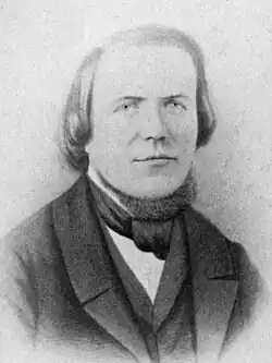 Head and bust of a man with a high forehead, hair reaching his shoulders, wearing a 19th-century three-piece suit and a cravat