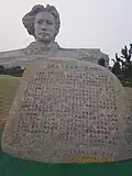 Inscrição na pedra e a estátua ao fundo.