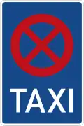 rechteckiges Schild mit blauem Grund, das oben einen roten Kreis zeigt, der durch zwei rote Diagonalen in vier Viertel geteilt ist, darunter in weißer Schrift "TAXI"