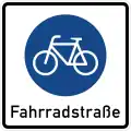 quadratisches Schild mit weißem Grund, darauf das Schild für Radweg (Fahrrad in blauem Kreis), darunter in schwarzer Schrift "Fahrradstraße"