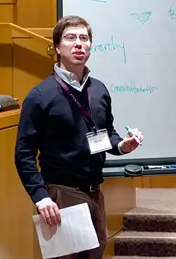 knee high portrait in sweater and slacks, holding papers in one hand and a marker in the other