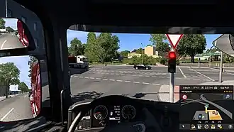 Tráfego de veículos visto a partir da primeira pessoa do motorista dentro da cabine do caminhão. No canto inferior direito há o GPS, à esquerda os retrovisores e ao centro o volante. O caminhão está parado no sinal.