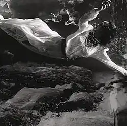 Em preto e branco, uma mulher de branco cai do céu em direção ao mar.