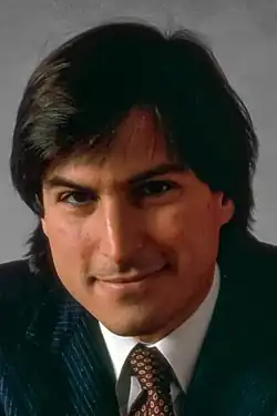 Steve Jobs sorrindo de terno escuro em 1984.