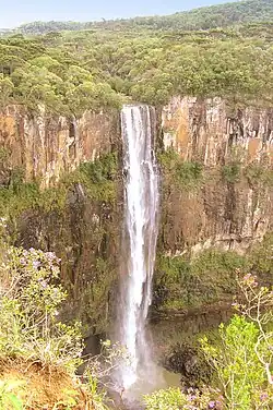 foto de uma cachoeira com uma grande queda d'água em um paredão de rocha basaltica e muita vegetação ao redor