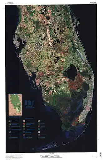 Imagem de satélite colorida da parte inferior da península da Flórida: grandes corpos d'água são pretos, a maior parte da terra ao sul do lago Okeechobee é vermelha, indicando a Área Agrícola dos Everglades; ao sul disso, há uma faixa azul escura mostrando onde os Everglades fluem em direção sudoeste até o Golfo do México