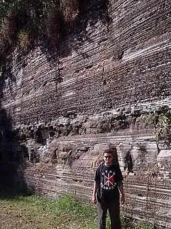 homem parado em frente a um paredão rochoso de rochas sedimentares