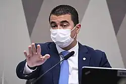 homem sentado falando ao microfone e gesticulando com a mão aberta