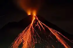 imagem de um vulcão ativo à noite com pequenas listras de escoamento de lava em sua encosta
