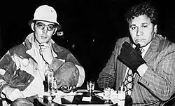 Photograph of two men seated at a table with drinks