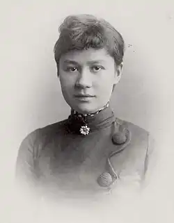 Uma fotografia, retrato em preto e branco à altura do peito, de uma jovem mulher com expressão leve