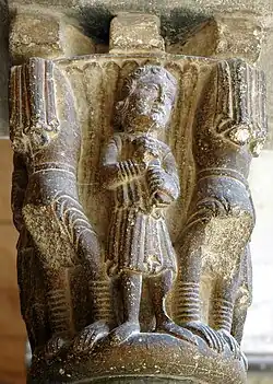 Um músico no centro de cada face toca crótalos ou dulzaina; nos ângulos, quatro jograis de cabeça para baixo apoiam as mãos no colarinho e os joelhos no denticulado. Capitel do claustro do mosteiro de Sant Cugat del Vallès, século XII.