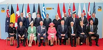 Sentados da esquerda para a direita estão: a Governadora-Geral da Nova Zelândia, Patsy Reddy, o presidente francês, Emmanuel Macron, a primeira-ministra britânica, Theresa May, o Príncipe Charles, a Rainha Elizabeth II, o presidente dos EUA, Donald Trump, o presidente grego, Prokopis Pavlopoulos, a chanceler alemã, Angela Merkel, e o primeiro-ministro holandês, Mark Rutte.