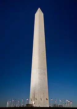 A dusk picture of the Washington Monument obelisk with flags around the base, in Washington, D.C.