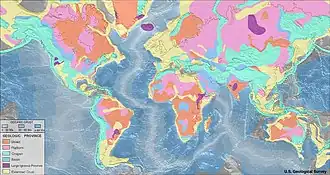 Imagem do mapa-mundi, nos continentes com as cores laranja, rosa, verde, azul, roxo e amarelo indicando as províncias geológicas; e na água, as cores cinza, azul claro e branco indicando a crosta oceânica.