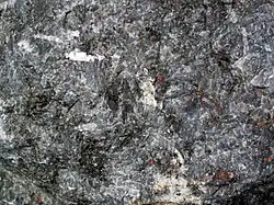 Imagem de uma rocha plutônica escura chamada gabro. A superfície tem aparência áspera, com cristais visíveis em tons de preto, cinza e branco. Os minerais estão misturados de forma irregular, formando uma textura granular típica de rochas que se formam lentamente no interior da Terra.