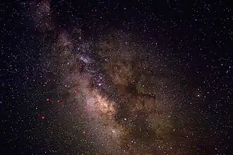 Uma visão do céu noturno perto de Sagittarius, aprimorada para mostrar melhor contraste e detalhes nas faixas de poeira. As principais estrelas em Sagittarius são indicadas em vermelho