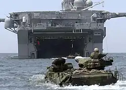 foto colorida de AAVs nadando se aproximando do convés de um navio de assalto anfíbio