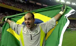 Um homem com feição de alegria, com os braços abertos segurando a bandeira brasileira às suas costas.